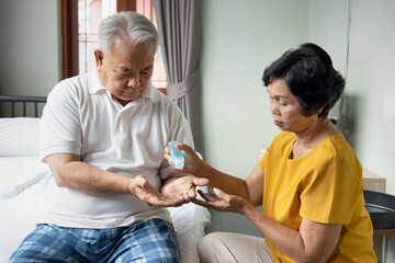 old senior wife giving alcohol gel hand sanitizer to her old senior husband, new normal senior man and woman social distancing healthy lifestyle in COVID-19 pandemic