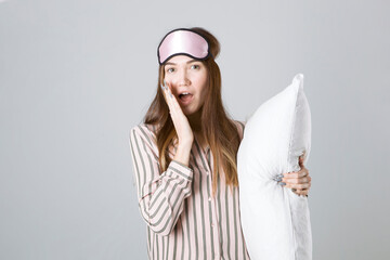 Beautiful young girl in a good mood in pajamas with a pillow in her hands on a light gray background