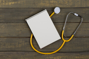 Medical and health care concept - yellow stethoscope and blank spiral notepad on wooden background