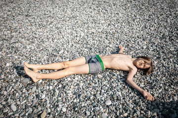 A thin white boy lies on the rocks with his eyes closed