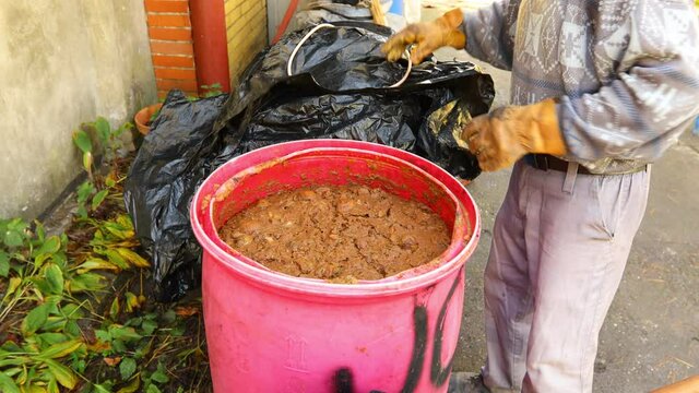 Man is mixing fruit marc made of chopped apples in plastic barrel using hoe. Shuffle process is for better fermenting alcohol, making alcoholic beverages such as brandy.