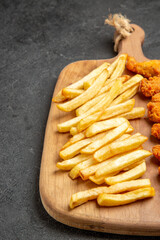Close up view of crispy and fried chicken meal on wooden cutting board on dark background