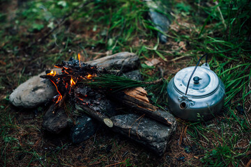 Camping kettle near small camp fire close-up. Cozy camping place in wild. Wonderful evening atmospheric background of campfire. Beautiful flame of small magic bonfire. Romantic warm place with fire.