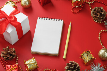 Christmas composition with notepad and a pencil for writing wishes with Christmas tree decorations on a red background.