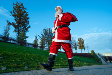 Obraz premium funny Santa Claus walking down the street with a bag of gifts