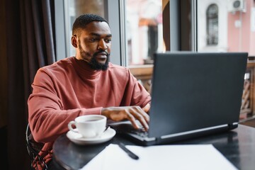 Portrait of happy african businessman sitting in a cafe and working on laptop