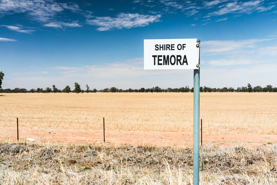 A sign post that reads "Shire of Temora" with a large empty field in farmland. Rural outback New South Wales, Australia.