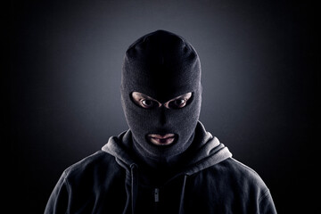 Criminal wearing black balaclava and hoodie in the dark - obrazy, fototapety, plakaty
