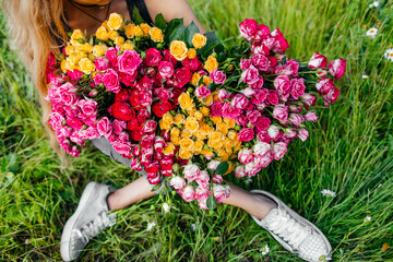 huge bouquet of colorful roses in the hands of a girl who sits on the grass. High quality photo