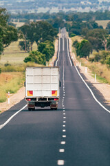 A freight haulage truck travels down a very long straight single lane paved road highway in rural New South Wales, Australia.