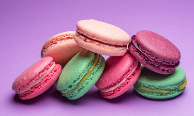 Colorful sweet macarons or macaroons, flavored cookies on purple background.