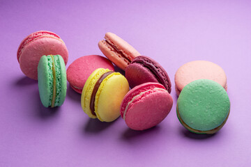 Colorful sweet macarons or macaroons, flavored cookies on purple background.