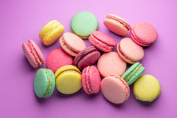 Colorful sweet macarons or macaroons, flavored cookies on purple background.