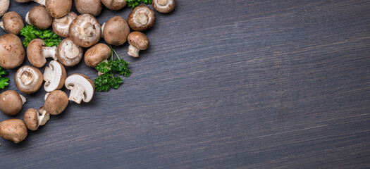 Brown colored edible mushrooms or cremini mushrooms on black table with herbs. Top view.
