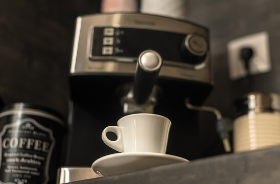 White Coffee Cup With Saucer On Kitchen Table With Modern Coffee Machine At Background. Modern Coffee Station At Home