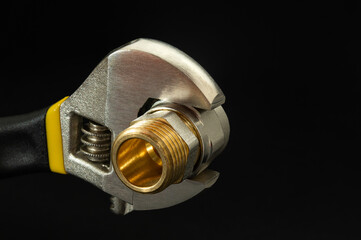 Adjustable wrench with brass fitting on black background. Plumbing repair idea