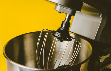 Chrome plated planetary mixer, whisk and bowl close up on yellow background, kitchen helper