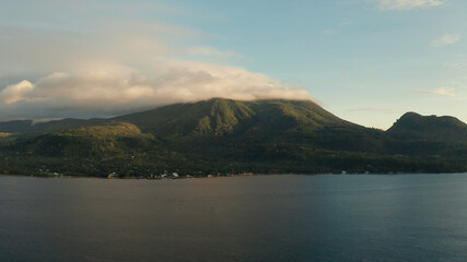 Coastline of tropical island covered with green forest against the blue sky with clouds at sunset, aerial view. Seascape: Ocean and sky.Philippines, Camiguin.