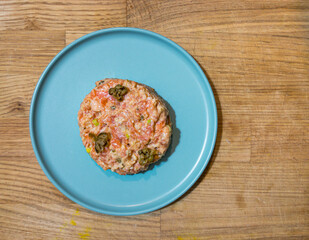 Salmon tartare with capers on plate on a wooden surface, top view