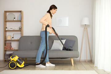 Beautiful young girl in a good mood makes house cleaning with a vacuum cleaner