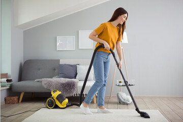 Beautiful young girl in a good mood makes house cleaning with a vacuum cleaner