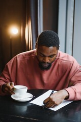 Young handsome dark-skinned businessman drinks coffee in a cafe.