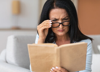 Senior confused woman in glasses trying to read book