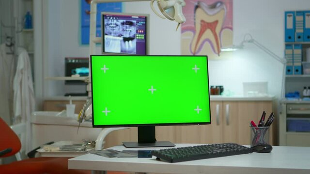 Computer with mockup display placed in front of camera in empty equipped stomatological room. Stomatology clinic with nobody in it prepared for patient using green screen, chroma key pc desktop