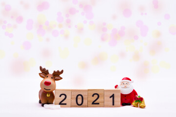 Merry Christmas and Happy New Year 2021. Number 2021 on small wooden slats. Ceramic Santa Claus standing gold bell, brown Reindeer smiling. On white background and sweet bokeh.