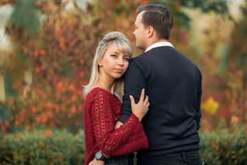 blonde girl in maroon sweater, brown-haired young man in blue sweater hug in the Park