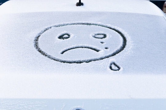 image of a crying face emoji on the snow on the back window of a car on a bright frosty winter day