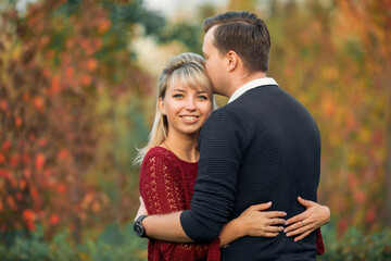 blonde girl in maroon sweater, brown-haired young man in blue sweater hug in the Park