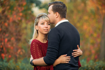 blonde girl in maroon sweater, brown-haired young man in blue sweater hug in the Park