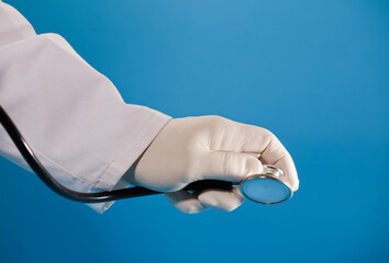 Stethoscope in doctor's hand with surgical glove and blue background.