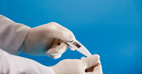 digital thermometer in doctor's hand with surgical glove and blue background.