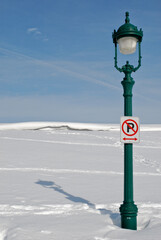 Lampadaire vert foncé au milieu d'un paysage de neige, de jour, avec un panneau "interdiction de stationner".