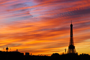 Silhouette de la tour Eiffel sur fond de coucher de soleil. Grande palette de couleurs, du bleu au rouge en passant par le rose et l'orange.