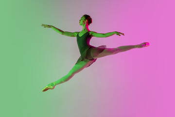 Flying. Young and graceful ballet dancer isolated on gradient pink-green studio background in neon....