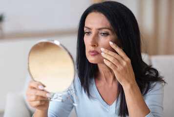 Mature woman checking her face in mirror, touching face
