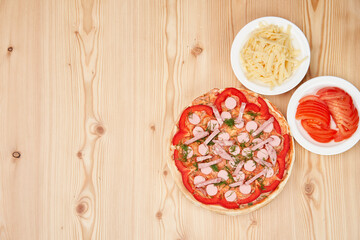 pizza on a wooden table with chopped tomato and cheese. Top view with copy space.