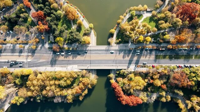 A road over the the lake with moving cars in the Titan park, multiple greenery. View from the drone, Bucharest, Romania