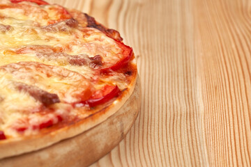 Hot, ready-made pizza with tomato on a wooden board. Homemade food. Side view with copy space.