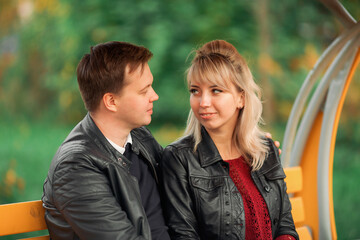 A young couple-brown-haired and blonde-sit on a bench and hold hands