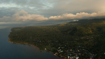 Coastline of tropical island covered with green forest against the blue sky with clouds and blue sea, aerial view. Seascape: Ocean and sky.Philippines, Camiguin.
