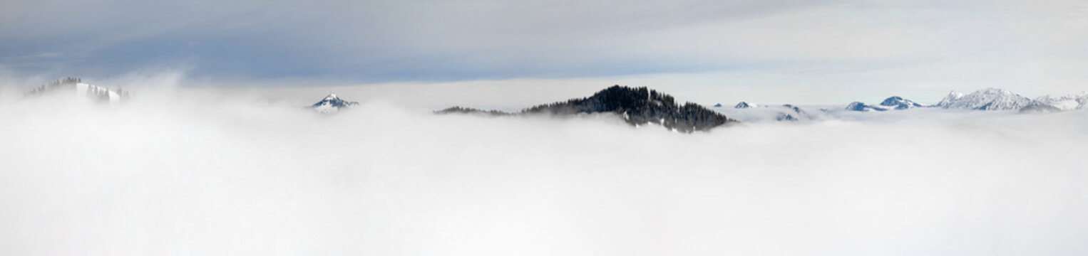 Winter Panoramic View to snow covered mountains above the clouds of inversion fog. View from Riedberger Horn in Allgau, Bavaria, Germany.