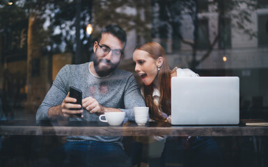 Amazed couple watching smartphone in cafe