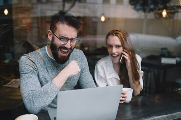 Euphoric young couple watching on laptop while sitting in cafe