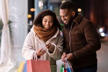 Happy afro couple using smartphone with many shopping bags