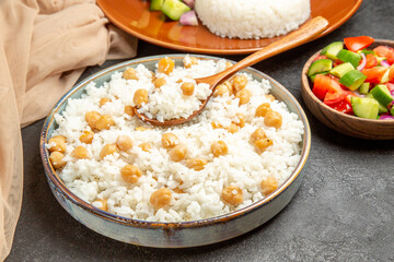 Peas and rice dish with a spoon and salad with tomato and cucumber and towel on dark table
