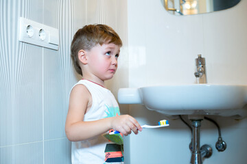 Little boy stands near the sink with a toothbrush. Boy brushing teeth with a toothbrush in the bathroom. 